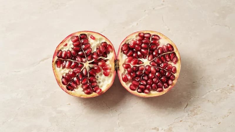 Halbierter Granatapfel auf hellem Kalkstein, eine Seite der Kernfläche natürlich gewachsen, die andere gleichmäßig gerastert