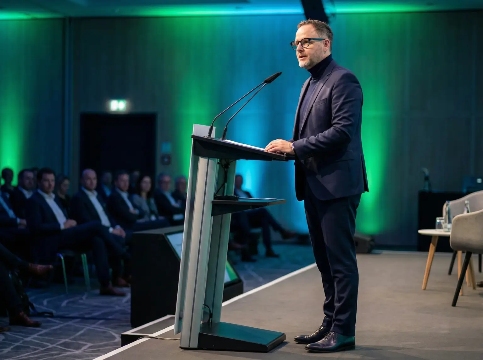 Oliver Range hält eine Rede am Rednerpult vor Publikum in modernem Konferenzsaal mit grün-blauer Beleuchtung