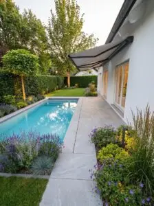 Moderner Pool mit Steinplatten, Markise und bepflanztem Garten neben Einfamilienhaus bei Abendlicht