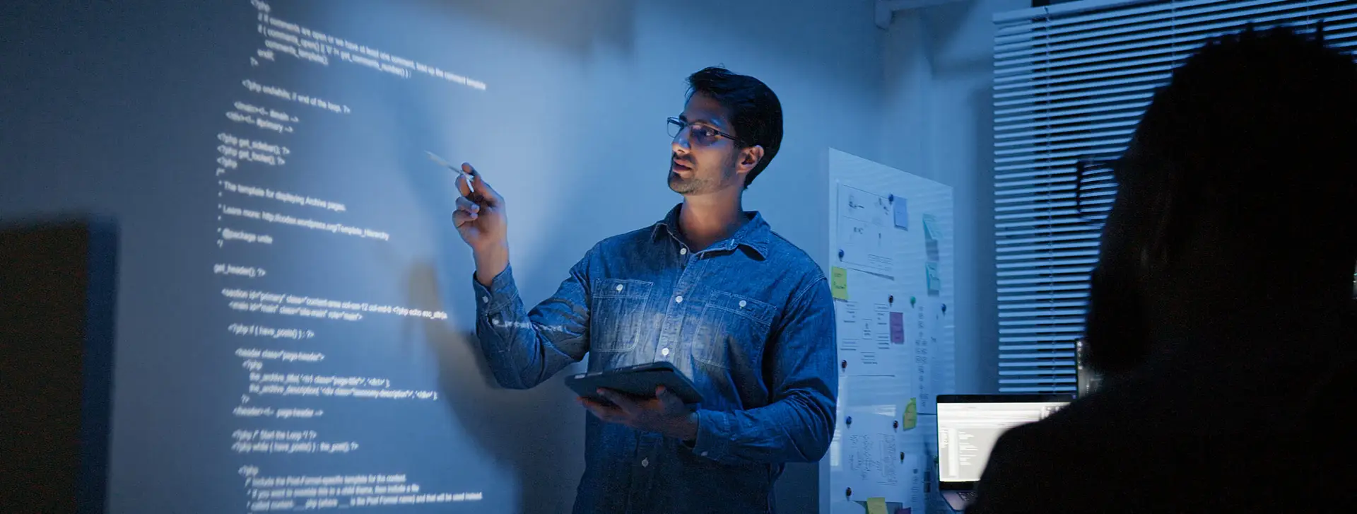 Entwickler präsentiert Programmcode an projizierter Wand mit Tablet im modernen Büro