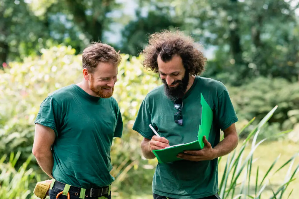 Two gardeners discuss a garden project outdoors and note details on a clipboard