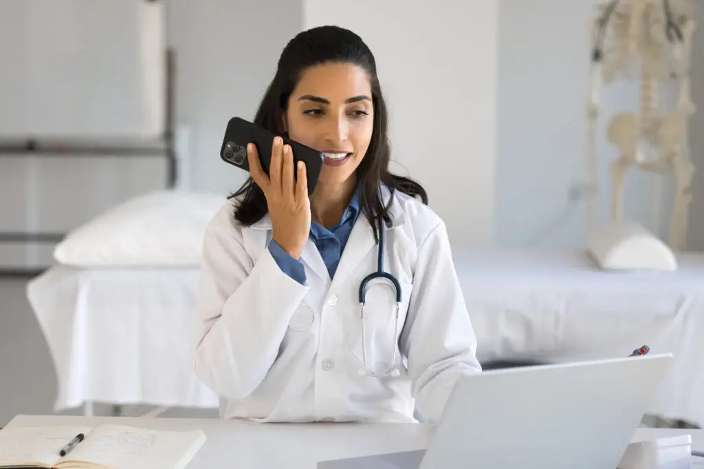 Ärztin diktiert über Smartphone im Behandlungszimmer mit Laptop