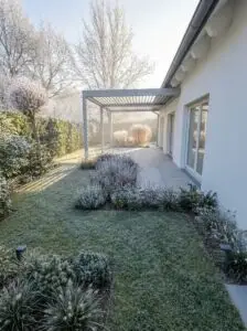 Moderner Garten mit Raureif, Pergola, Terrasse, Rasen, Stauden und Gräsern im Morgenlicht