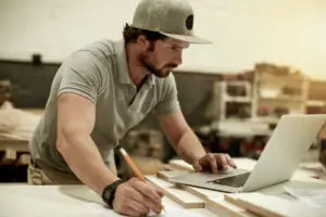 Tradesperson working in a workshop with a laptop, pencil, and cut wooden panels
